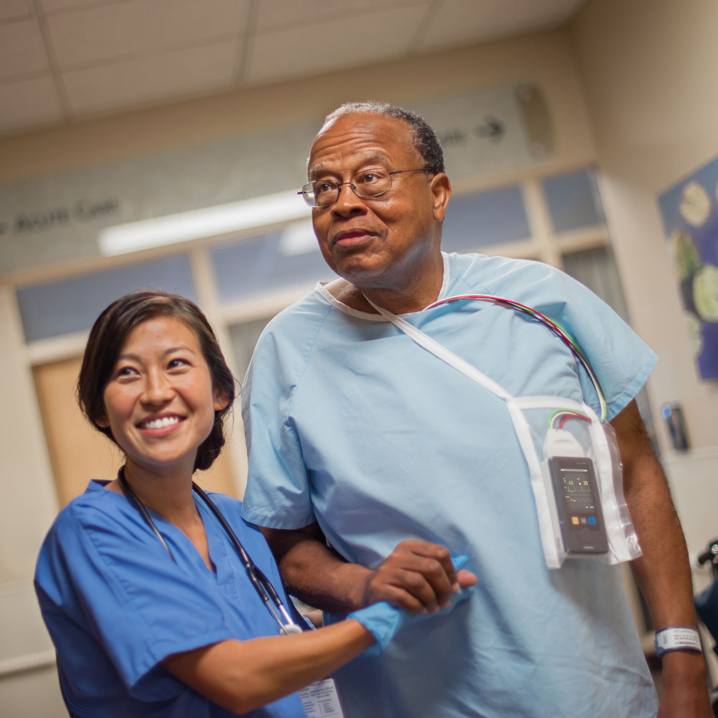 一位医疗保健专业人员握着一位穿着病号服、身上戴着监护设备的患者的手