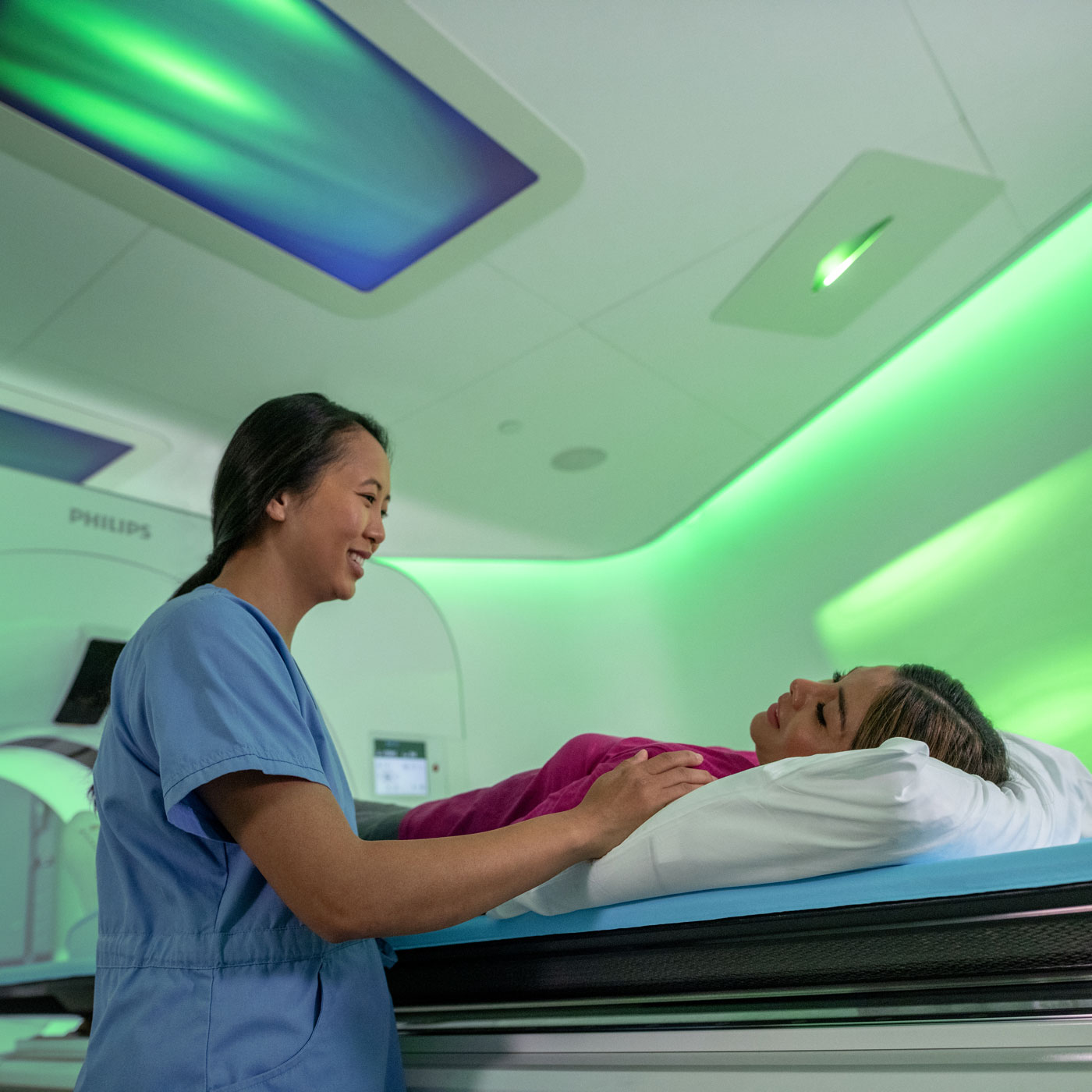 医护人员微笑着看着平躺在成像设备前的患者